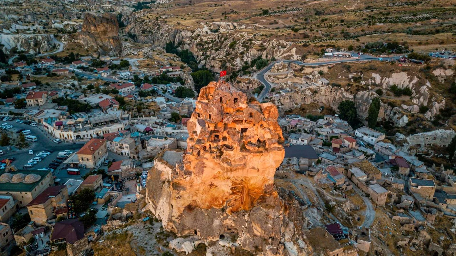 Uçhisar castle glowing at sunset above the village in Cappadocia, with no balloons in the evening sky