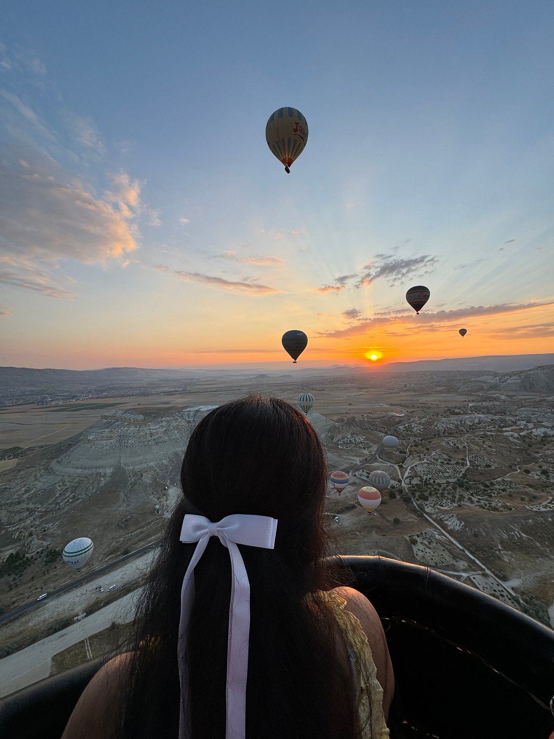 A guest watches the sunrise from a Cappadocia balloon basket as dozens of other balloons rise across Göreme valley