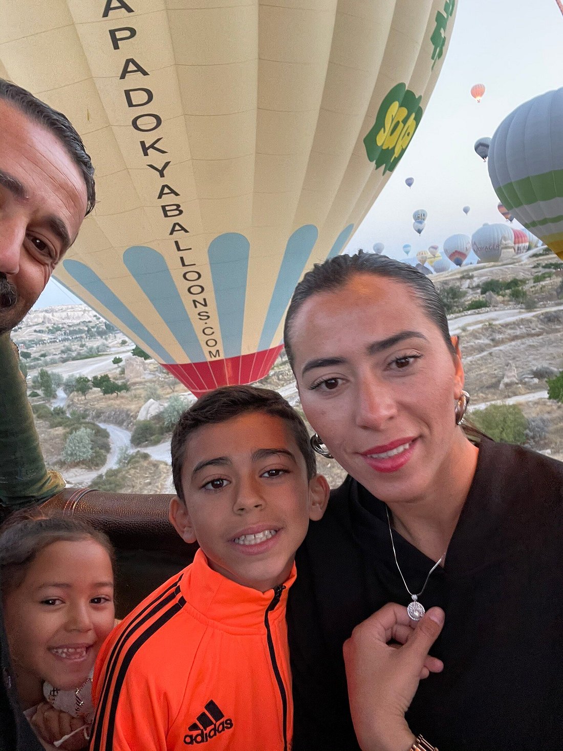 A family enjoys their hot air balloon ride above Cappadocia, surrounded by other balloons at sunrise