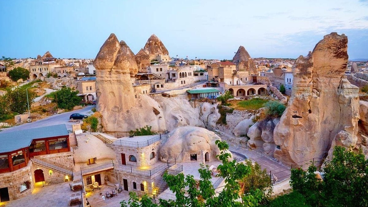 Göreme at twilight, with cave hotels built into the rock walls and fairy chimneys rising directly above the village
